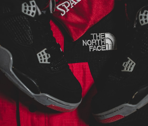 Black athletic shoes are placed alongside red and black sportswear bearing logos from Spalding and The North Face.