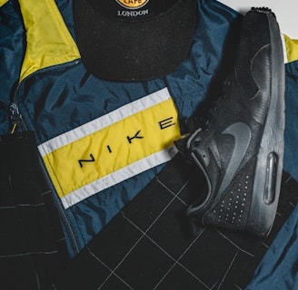A Hard Rock Cafe London cap, a Nike sports jacket with a yellow, white, and blue color scheme, and a black Nike shoe are arranged. The items are laid out on a flat surface, showcasing a mix of casual and sporty attire.