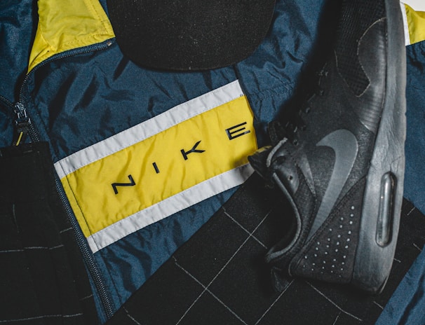 A Hard Rock Cafe London cap, a Nike sports jacket with a yellow, white, and blue color scheme, and a black Nike shoe are arranged. The items are laid out on a flat surface, showcasing a mix of casual and sporty attire.