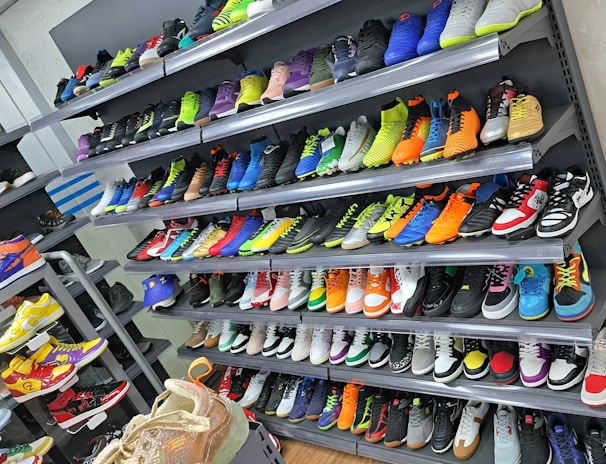 A display of various colorful athletic shoes neatly arranged on multiple shelves. The shoes come in a variety of designs and colors, including neon greens, blues, oranges, and vibrant patterns.